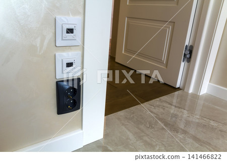 Modern house interior with warm floor controller panels on the wall, wooden parquet and white door Modern house interior with warm floor controller panels on the wall, wooden parquet and white door 141466822