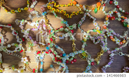 Colorful handmade beaded floral bracelets on wooden table in bright sunlight Colorful handmade beaded floral bracelets on wooden table in bright sunlight 141466983