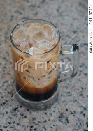 top view Iced black coffee with milk, served in a large handled glass mug and placed on a marble surface background, cool, food, drink, sweet, copy space top view Iced black coffee with milk, served in a large handled glass mug and placed on a marble surface background, cool, food, drink, sweet, copy space 141467904