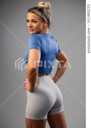 Fit woman in blue crop top and gray athletic shorts posing confidently in studio Fit woman in blue crop top and gray athletic shorts posing confidently in studio 141468255