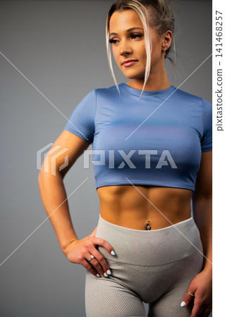 Fit woman in blue crop top and gray leggings showing toned abs with hand on hip Fit woman in blue crop top and gray leggings showing toned abs with hand on hip 141468257