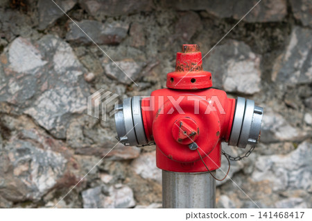Red fire hydrant mounted on metal pole against a textured stone wall background 141468417