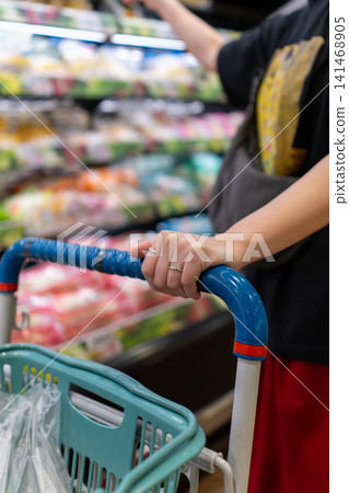 A woman's hands and shopping cart as she buys daily necessities and groceries. A woman's hands and shopping cart as she buys daily necessities and groceries. 141468905