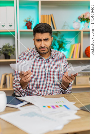 Indian man on home table stressed by bills and payments while using laptop for money budget planning Indian man on home table stressed by bills and payments while using laptop for money budget planning 141469403