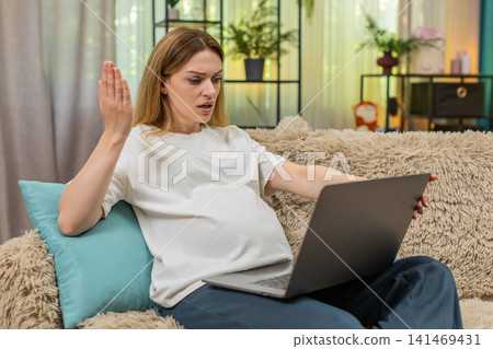 Pregnant woman frustrated as laptop freezes waves hand moves device aside upset working at home sofa Pregnant woman frustrated as laptop freezes waves hand moves device aside upset working at home sofa 141469431