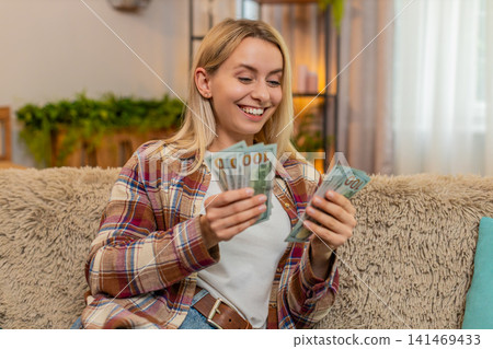 Woman counting cash money at home, smiling proudly while planning budget after lottery win or raise Woman counting cash money at home, smiling proudly while planning budget after lottery win or raise 141469433