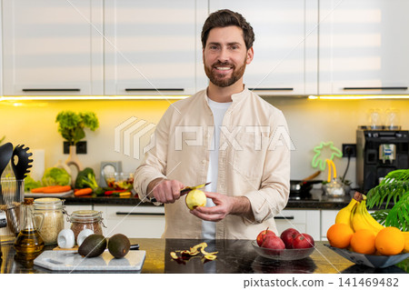 Middle-aged man in headphones peeling apple singing dancing in home kitchen for healthy diet music Middle-aged man in headphones peeling apple singing dancing in home kitchen for healthy diet music 141469482