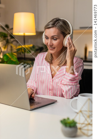 Adult woman in headphones tweaks layout on laptop moves layers nods to music smiles saves version Adult woman in headphones tweaks layout on laptop moves layers nods to music smiles saves version 141469773