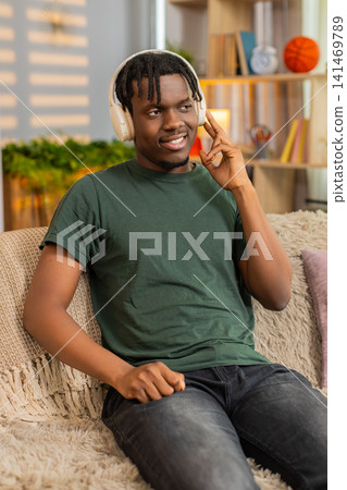 African American young man on home sofa listening to music in headphones with calm smile close up African American young man on home sofa listening to music in headphones with calm smile close up 141469789