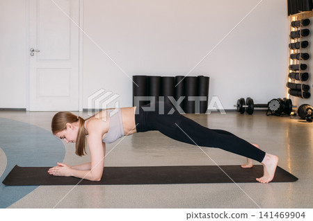 Plank strength. Physical therapy. Young woman in sportswear hand pushing up on floor mat in gym with professional sport equipment. Plank strength. Physical therapy. Young woman in sportswear hand pushing up on floor mat in gym with professional sport equipment. 141469904