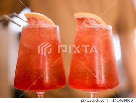 Garnishing drink. Bartender service. Man adding with tweezers grapefruit slice in glass. Bright spritz cocktail with bubbles citrus fruit piece. Garnishing drink. Bartender service. Man adding with tweezers grapefruit slice in glass. Bright spritz cocktail with bubbles citrus fruit piece. 141469909