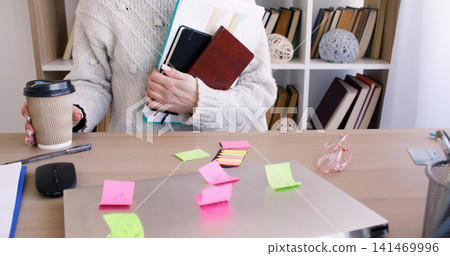 Coffee break. Freelancer lifestyle. Unrecognizable female using notebook at office desk with laptop at professional workplace. Coffee break. Freelancer lifestyle. Unrecognizable female using notebook at office desk with laptop at professional workplace. 141469996