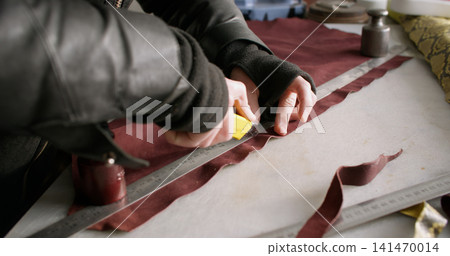 Footwear manufacturing. Shoes factory. Unrecognizable craftsman hands using stationery knife metal ruler cutting material at workspace. Footwear manufacturing. Shoes factory. Unrecognizable craftsman hands using stationery knife metal ruler cutting material at workspace. 141470014