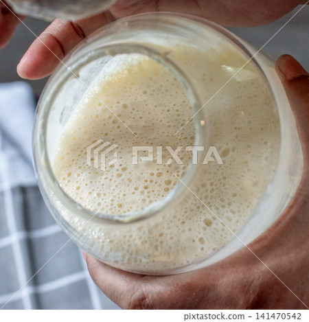 Close-up of an active sourdough starter showing natural fermentation bubbles inside a glass jar. Authentic homemade bread baking, wild yeast culture, and artisan baking process. 141470542
