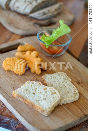Fresh artisan bread served with crispy chicken nuggets and a simple salad on a rustic wooden cutting board. Cozy homemade breakfast, snack or family meal with natural light. Fresh artisan bread served with crispy chicken nuggets and a simple salad on a rustic wooden cutting board. Cozy homemade breakfast, snack or family meal with natural light. 141470543