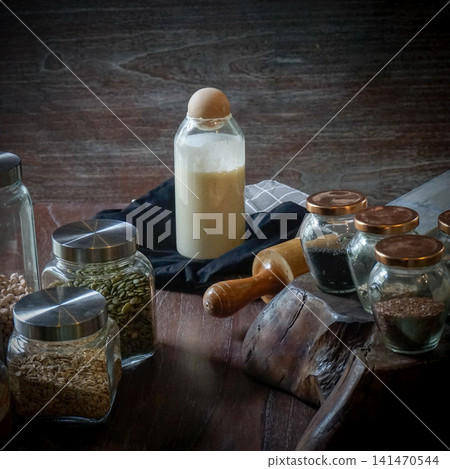 Rustic Sourdough Starter in Glass Jar with Baking Grains and Seeds, Natural Fermentation for Artisan Homemade Bread Rustic Sourdough Starter in Glass Jar with Baking Grains and Seeds, Natural Fermentation for Artisan Homemade Bread 141470544