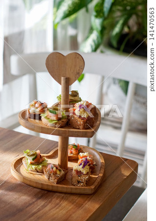 Heart Shaped Wooden Tiered Serving Stand with Assorted Gourmet Canapes Finger Food Appetizers on Rustic Wooden Table in Cozy Cafe Setting Heart Shaped Wooden Tiered Serving Stand with Assorted Gourmet Canapes Finger Food Appetizers on Rustic Wooden Table in Cozy Cafe Setting 141470563