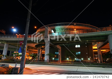 A massive, loop-shaped highway junction and the city lights floating in the night sky. A massive, loop-shaped highway junction and the city lights floating in the night sky. 141470742