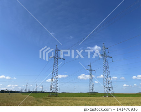 High voltage electricity transmission towers across green farmland with power lines under blue sky High voltage electricity transmission towers across green farmland with power lines under blue sky 141470936