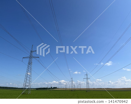 High voltage electricity transmission towers with power lines across green fields under blue sky 141470942