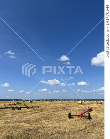 Farm trailers in harvested field with round hay bales under clear blue summer sky landscape Farm trailers in harvested field with round hay bales under clear blue summer sky landscape 141470944
