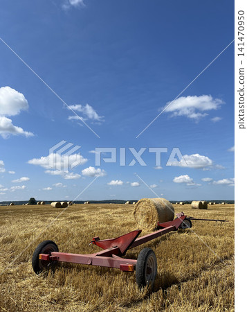 Header trailer with round hay bale in harvested farmland under clear blue summer sky landscape Header trailer with round hay bale in harvested farmland under clear blue summer sky landscape 141470950