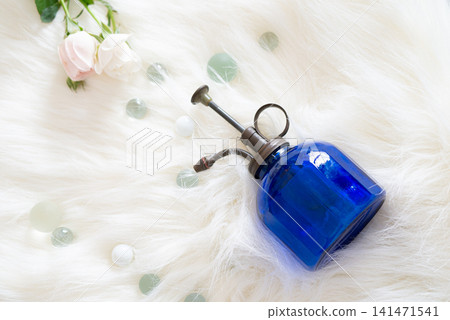 一個藍色噴霧瓶、一些彈珠和玫瑰花放在人造毛皮上。 一個藍色噴霧瓶、一些彈珠和玫瑰花放在人造毛皮上。 141471541
