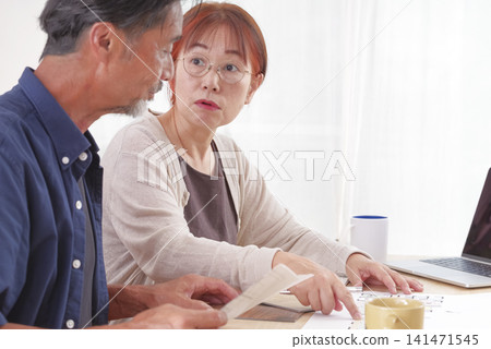 一對老年夫婦一邊查看房屋設計圖一邊討論。 一對老年夫婦一邊查看房屋設計圖一邊討論。 141471545