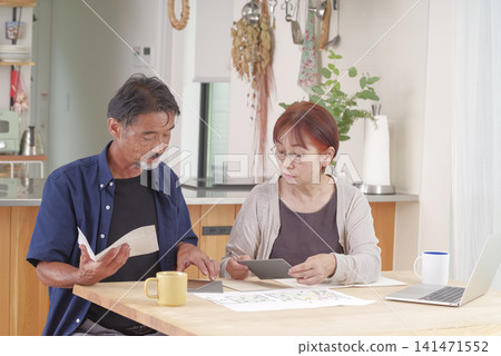一對老年夫婦一邊查看房屋設計圖一邊討論。 一對老年夫婦一邊查看房屋設計圖一邊討論。 141471552