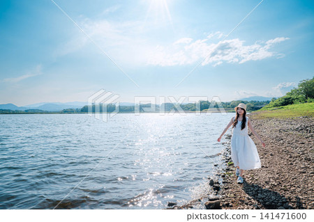 一位女子沿著湖邊行走，湖面波光粼粼。 141471600