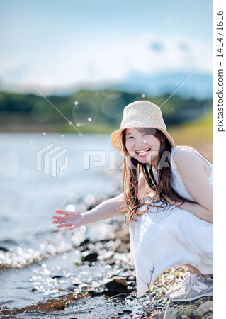 A woman in a straw hat splashes water by the lake. A woman in a straw hat splashes water by the lake. 141471616
