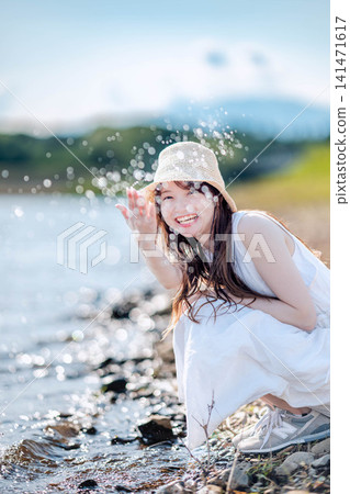 一位身穿白色洋裝的女子在水邊嬉戲玩耍。 一位身穿白色洋裝的女子在水邊嬉戲玩耍。 141471617