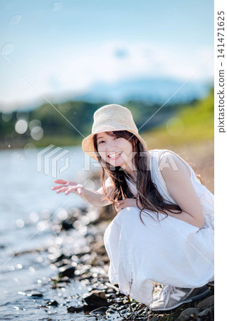 一位身穿白色洋裝的女子在湖岸邊潑水。 一位身穿白色洋裝的女子在湖岸邊潑水。 141471625