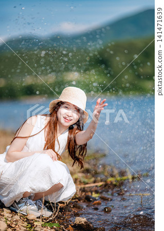 一位戴著草帽的女子在波光粼粼的海濱潑水。 一位戴著草帽的女子在波光粼粼的海濱潑水。 141471639
