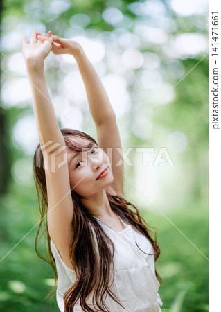A woman stretches and relaxes in a forest of fresh greenery. A woman stretches and relaxes in a forest of fresh greenery. 141471661