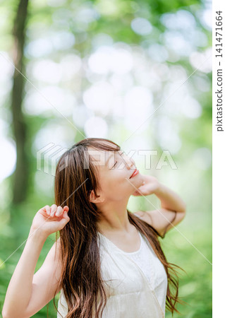 A woman in a white dress, with her hand on her neck, looks up in the forest. A woman in a white dress, with her hand on her neck, looks up in the forest. 141471664