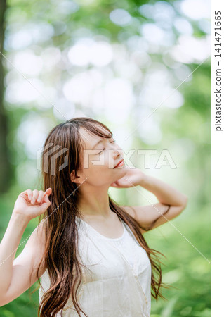一位年輕女子放鬆地撫摸著頭髮,背景是鬱鬱蔥蔥的綠植。 一位年輕女子放鬆地撫摸著頭髮,背景是鬱鬱蔥蔥的綠植。 141471665