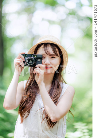 A woman smiles, holding a film camera in a forest of fresh greenery. A woman smiles, holding a film camera in a forest of fresh greenery. 141471672