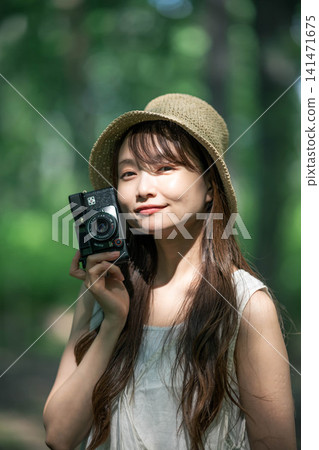 A woman in a straw hat holding a film camera in the forest. A woman in a straw hat holding a film camera in the forest. 141471675
