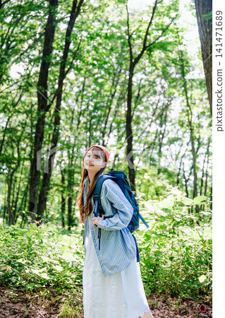A woman in a denim shirt looks back in a lush green forest. A woman in a denim shirt looks back in a lush green forest. 141471689