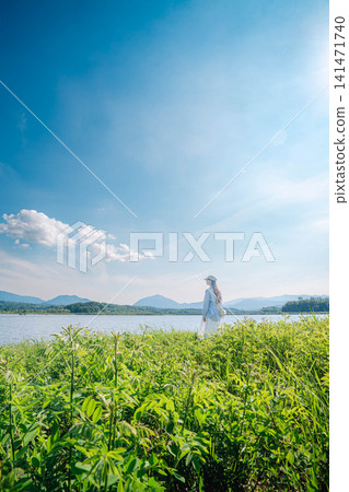 一位女子站在明媚的夏日天空下的湖邊。 一位女子站在明媚的夏日天空下的湖邊。 141471740