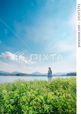 一位女子背對著鏡頭,仰望著湖邊草地上的夏日天空。 一位女子背對著鏡頭,仰望著湖邊草地上的夏日天空。 141471741