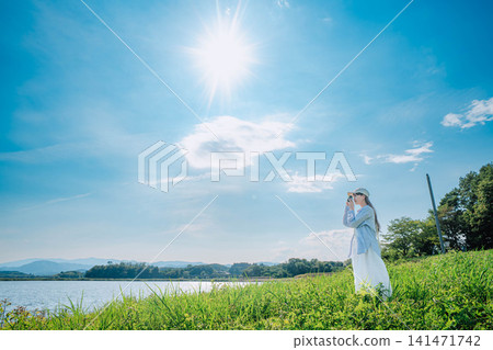 陽光和藍天下，一位女子在草地上凝望著湖泊。 141471742
