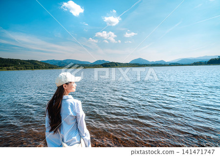 A woman in a white dress stands by the lake, gazing into the distance. 141471747