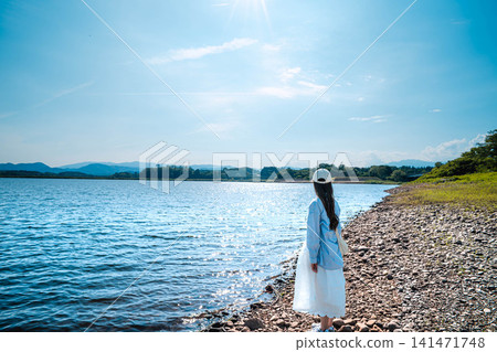 A woman standing by the lake in the summer sun. A woman standing by the lake in the summer sun. 141471748