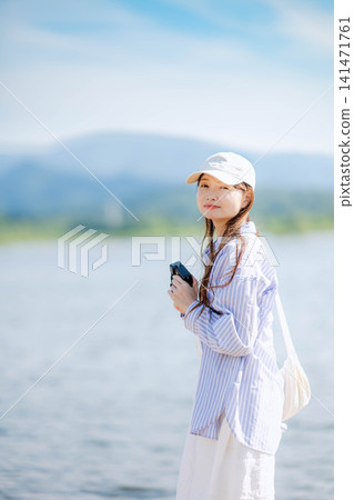 湖邊站著一位戴著白色帽子的女子,手裡拿著一台底片相機。 湖邊站著一位戴著白色帽子的女子,手裡拿著一台底片相機。 141471761