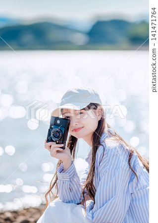 A woman in a white hat takes a photograph by the lake. A woman in a white hat takes a photograph by the lake. 141471764