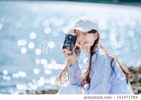 一位戴著白色帽子的女子微笑地透過湖邊的相機鏡頭看著窗外。 141471769