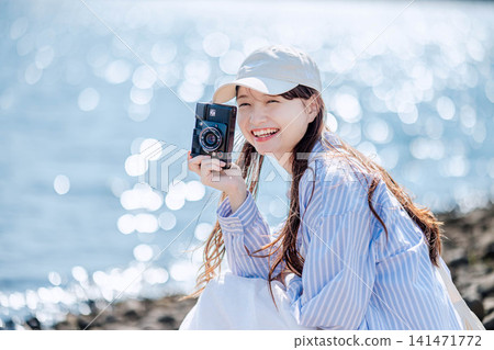 一位女士面帶微笑,手持相機站在波光粼粼的湖邊。 一位女士面帶微笑,手持相機站在波光粼粼的湖邊。 141471772