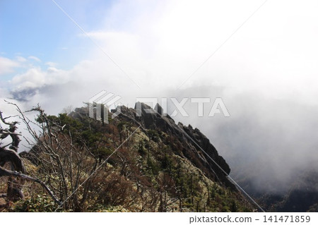 A spectacular view of the sharp, sheer rocky peaks of Tengudake, the highest peak of the Ishizuchi Mountain Range in Ehime Prefecture, against a clear blue sky, as seen from the southern peak. A spectacular view of the sharp, sheer rocky peaks of Tengudake, the highest peak of the Ishizuchi Mountain Range in Ehime Prefecture, against a clear blue sky, as seen from the southern peak. 141471859